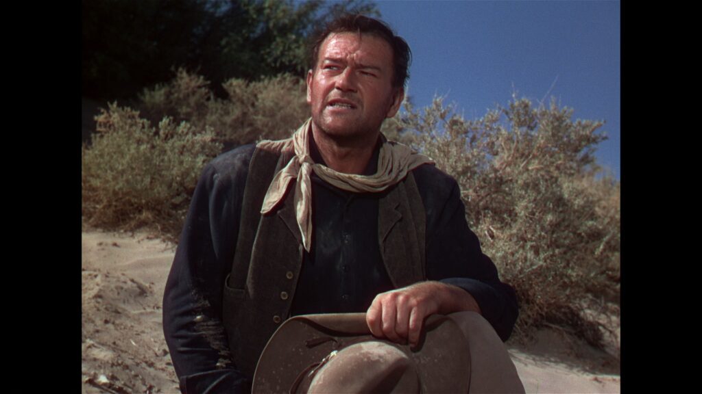 Robert, gespielt von John Wayne, ist in Spuren im Sand sichtlich erschöpft.