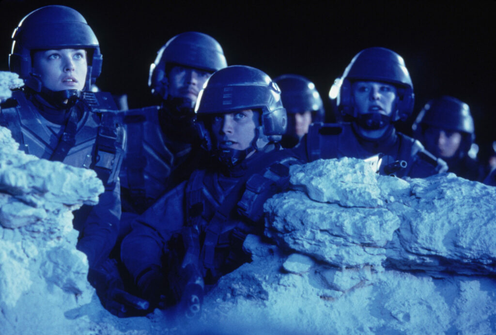 Auf dem Bild sieht man die namensgebenden "Starship Troopers", die sich im Dunklen hinter einer kleinen Felsformation befinden. Dabei beobachten sie etwas außerhalb des Bildes.