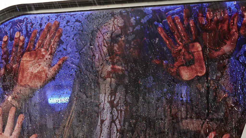 Hinter der blutverschmierten Scheibe des Buses sieht man Hände und ein Opfer, das sich gegen die Scheibe drückt - Texas Chainsaw Massacre.