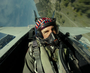 Ein Jetpilot fliegt schräg zum Boden. Auf dem Helm ist der Schriftzug Maverick zu erkennen.