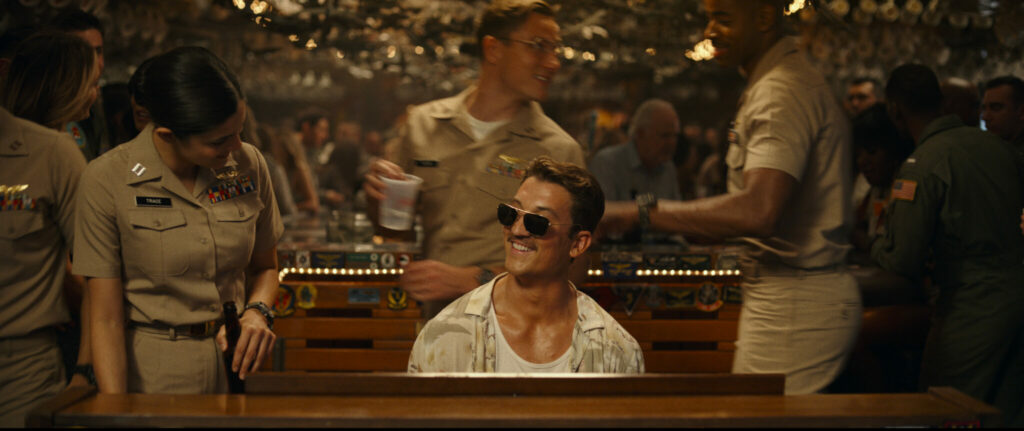 Ein Mann mit Sonnenbrille und Navy-Uniform sitzt am Klavier. Er trägt auf der Nase eine Sonnenbrille. Es ist der Schauspieler Miles Teller im Film Top Gun 2: Maverick.