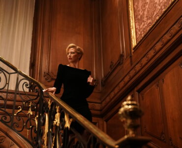 Allison O'Hara (Carrie Coon) in einem Treppenhaus. Sie trägt ein schwarzes Abendkleid.