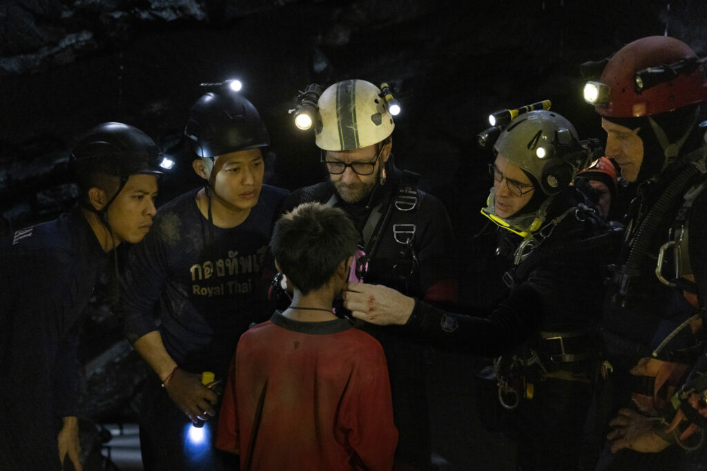 Mehrere mit Helmen, Taschenlampen und Seilen ausgerüstete Rettungshelfer haben einen der kleinen Jungen entdeckt in Dreizehn Leben - Neu bei Prime im August 2022