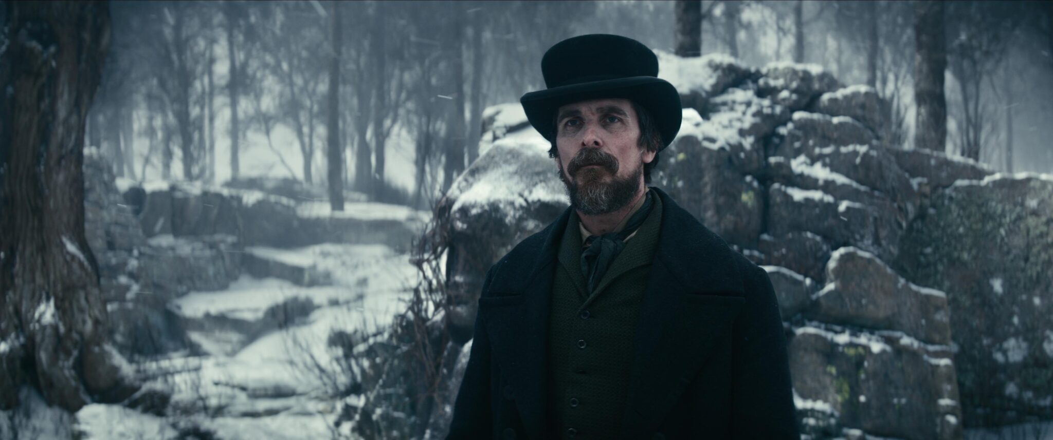 Christian Bale steht in einer verschneiten Szenerie vor einer Steinmauer mit dunklem Mantel über dunkelgrünem Jackett. Der denkwürdige Fall des Mr. Poe