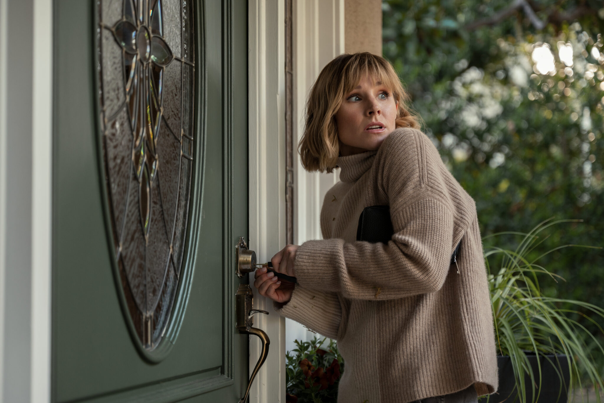 Kristen Bell versucht eine grüne Eingangstür mit Werkzeugen zu öffnen. Dabei blickt sie vorsichtig hinter sich. The Woman in the House Across the Street from the Girl in the Window.