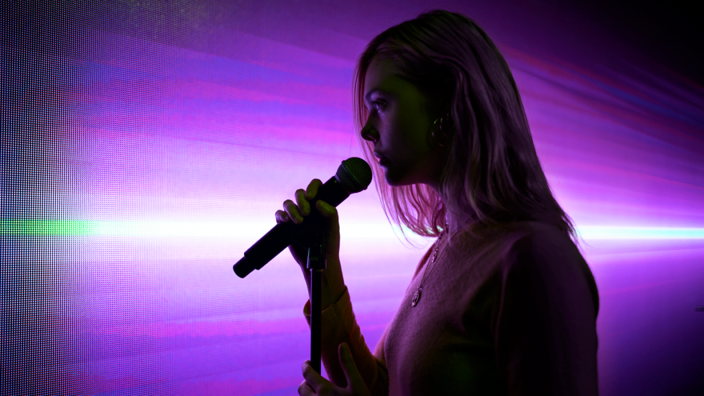 Violet (Elle Fanning) singt auf einer passend violett beleuchteter Bühne.