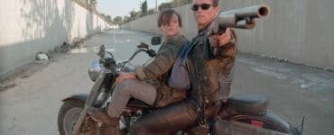 John Connor (Edward Furlong) und der T-800-Terminator (Arnold Schwarzenegger) sitzen in "Terminator 2" auf einem Motorrad. Der Terminator hat eine Schrotflinte auf die Kamera gerichtet.