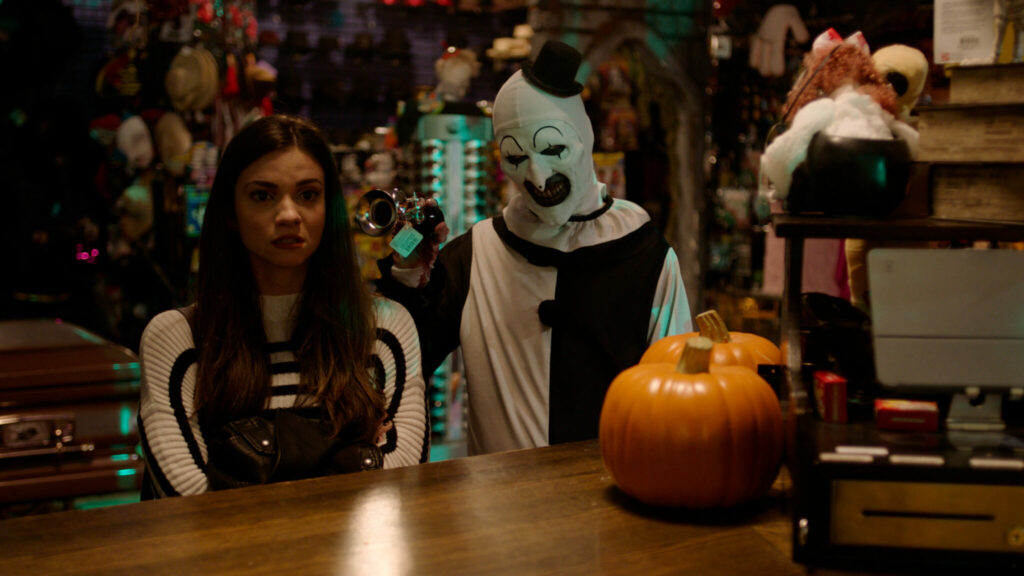 David Howard Thornton als Art nervt Lauren LaVera als Sienna in Terrifier 2 it seiner Hupe, während beide im Halloweenshop an der Kasse warten.