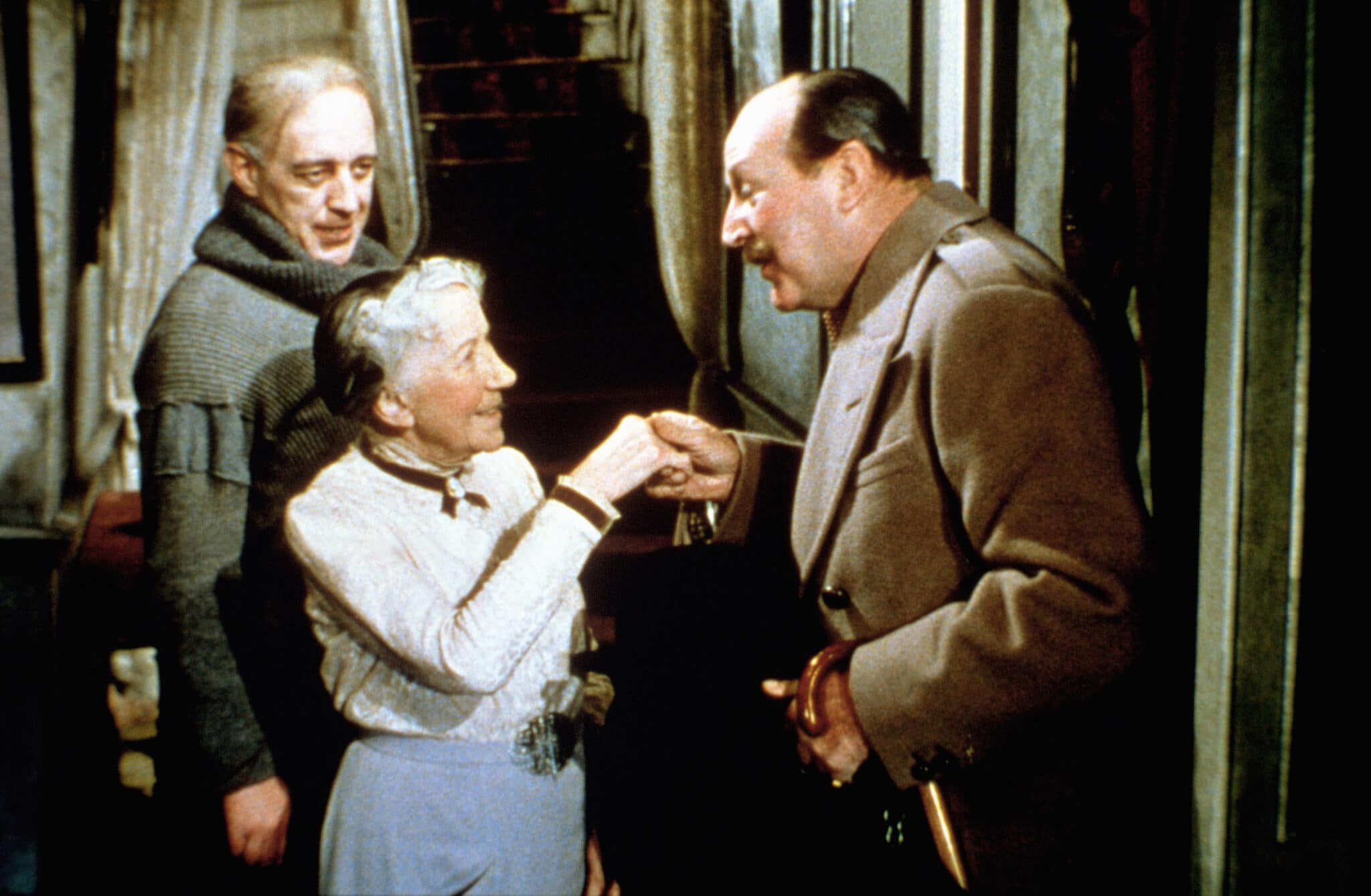 Major Courtney (Cecil Parker) begrüßt Mrs. Wilberforce (Katie Johnson) in Ladykillers vornehm in ihrem Haus. Im Hintergrund steht der schelmisch dreinblickende Professor Marcus (Alec Guinness).