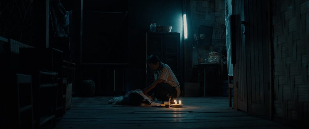 In seiner schattigen Hütte hockt der alte Mann über der schlafenden Mina, neben ihnen brennt eine Kerze - The Long Walk.
