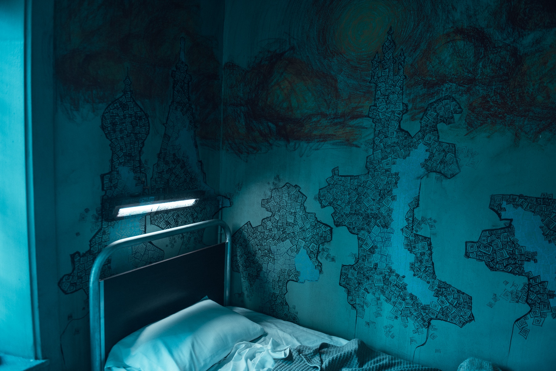 Ein Krankenhausbett in der Ecke eines leeren Zimmers, dessen Wände mit kryptischen Zeichnungen vollgekritzelt sind, in "The New Mutants".