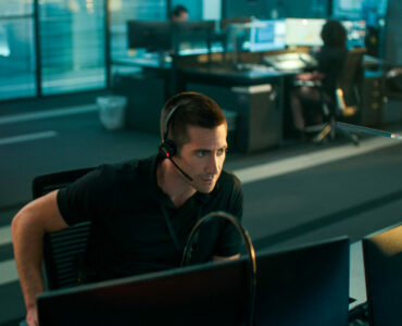 Jake Gyllenhaal in der Rettungszentrale vor zwei Flachbildschirmen mit Headset. Im Vordergrund sieht man eine rote Lampe leuchten