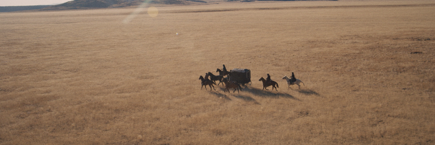 Eine Kutsche fährt über weites Land begleitet von mehreren Reitern.