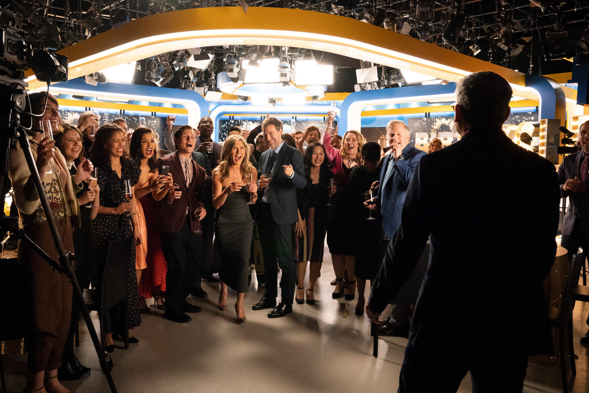 Ein Studio eines Fernsehsenders voller feiernder Menschen im Halbkreis stehend. Einige tragen Abendgarderobe und halten Sektgläser in den Händen.