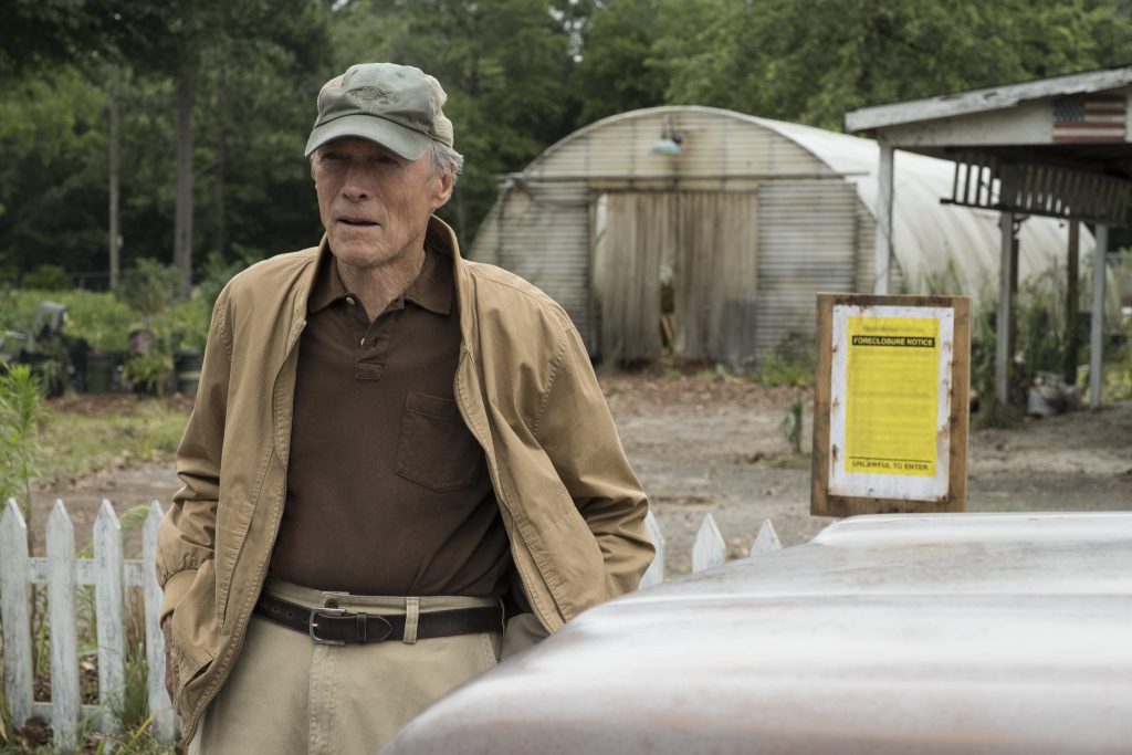 Clint Eastwood geht in seiner Rolle als Earl Stone von seinem Grundstück zu seinem Auto. Auf einem im Hintergrund noch zu sehenden Schild wird die Zwangsversteigerung seines besitzes angekündigt.