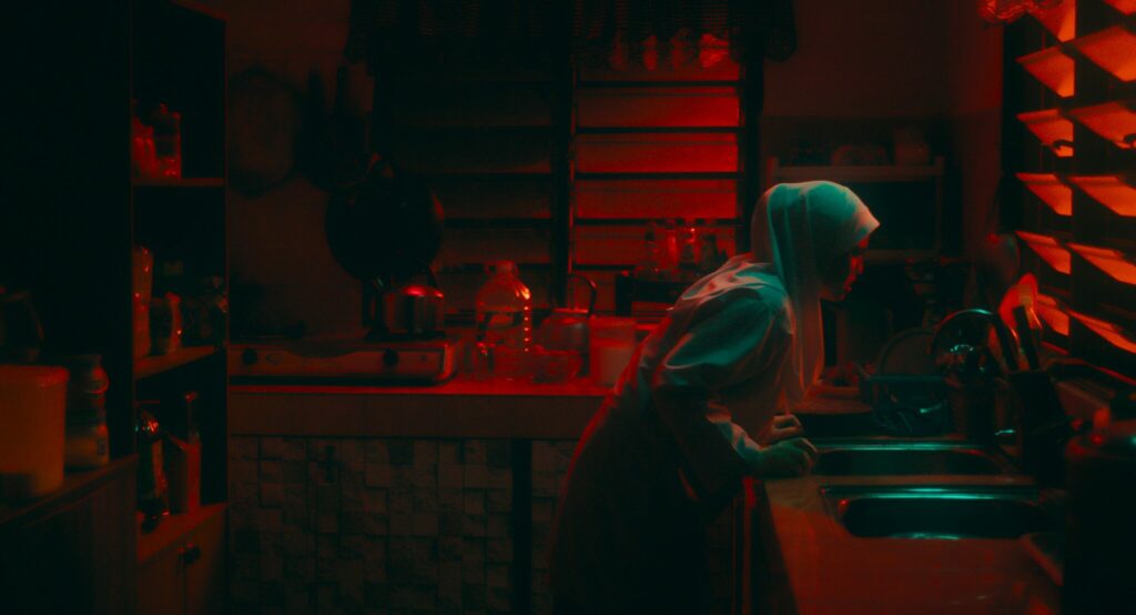 Eine junge Frau mit Kopftuch beugt über einem Waschbecken in einem in dunkles Rot getünchten Raum - Fantasy Filmfest 2023