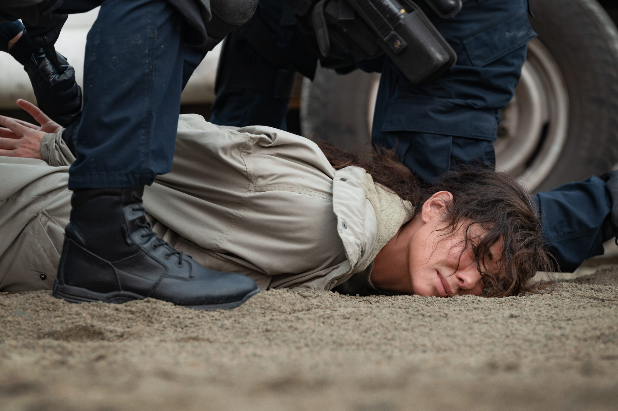 Sandra Bullock wird von bewaffneten Polizisten niedergestreckt und lieg auf einem sandigen Boden.