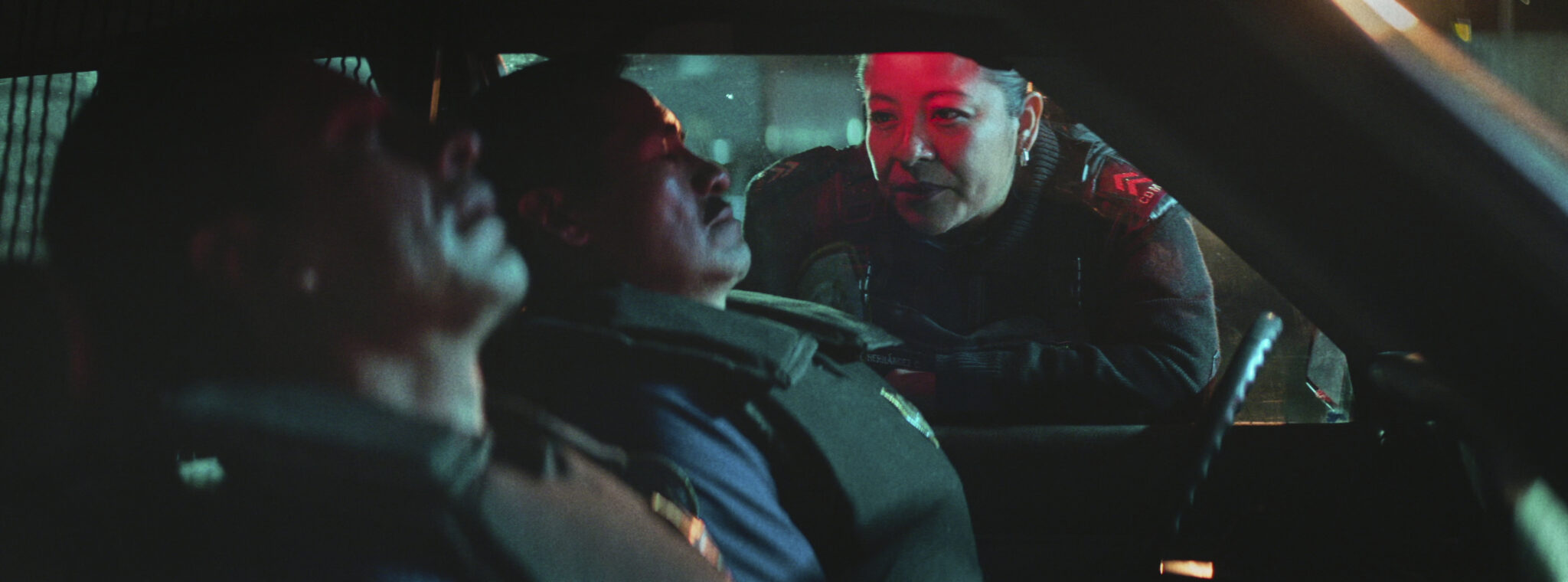 Eine Polizistin schaut durch ein Autofenster in ein Auto, in dem zwei Männer mit Schutzweste sitzen.