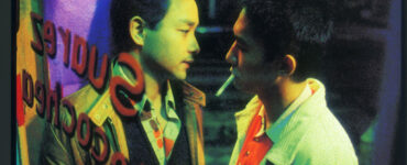 Ho Po-wing und Lai Yiu-fai eng zusammen hinter einer Glasfassade. Lai hat eine Zigarette zwischen den Lippen.