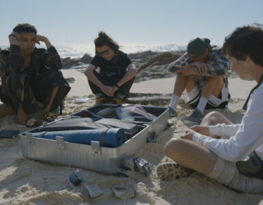 Vier Jugendliche sitzen in The Wilds am Strand vor einem offenen Koffer - neu auf Prime im Mai 2022.