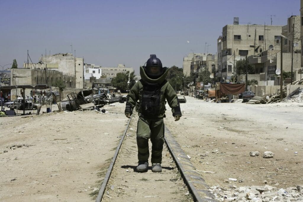 Ein Soldat im Schutzanzug läuft in einem menschenleeren Gebiet auf Zuggleisen auf die Kamera zu