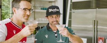 Ryan Reynolds und Rob McElhenney mit Trikots des AFC Wrexham und Cocktailgläsern in der Hand