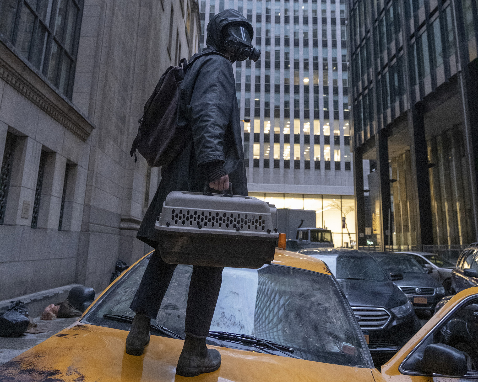 Eine Person steht mit Gasmaske auf einem Taxi in den Häuserschluchten von New York in Y: The Last Man.