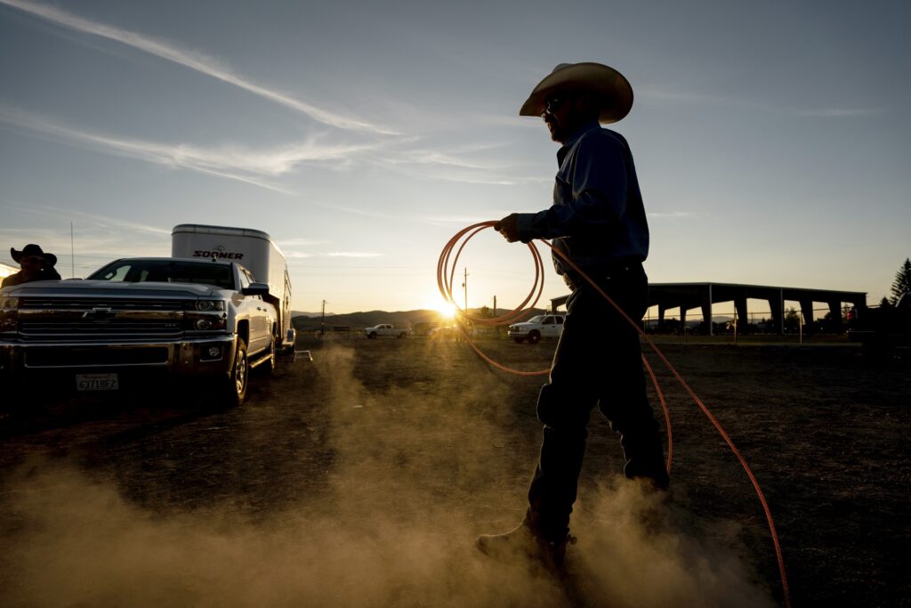 Am Rande eines Rodeos hantiert ein Cowboy mit einem Lasso, während ein Range Rover mit Pferdetransporter an ihm vorbeifährt.