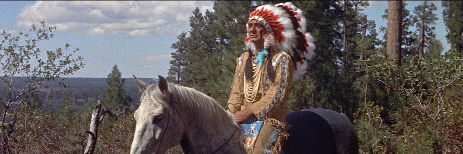 Häuptling Red Cloud, gespielt von Eduard Franz, sitzt in Zwischen zwei Feuern in vollem Federschmuck auf einem Pferd.