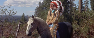 Häuptling Red Cloud, gespielt von Eduard Franz, sitzt in Zwischen zwei Feuern in vollem Federschmuck auf einem Pferd.