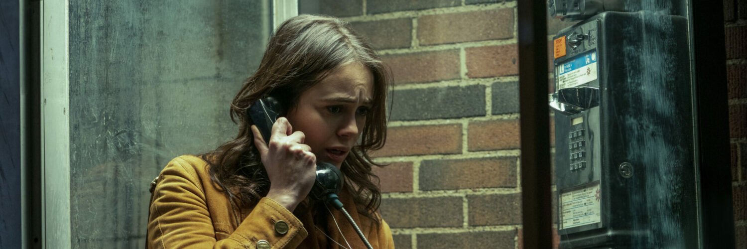 Melody (Dina Shihabi) telefoniert in einer Telefonzelle vor dem Visser-Gebäude und schaut besorgt aus in Archive 81