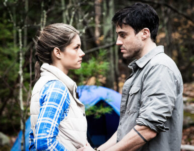 Die Hauptfiguren Jenn und Alex stehen vor ihrem Zelt im Wald und schauen sich an.