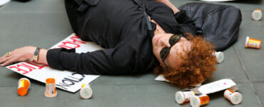 Nan Goldin liegt auf dem Boden eines Museums. Neben ihr liegen leere Medikamentendöschen und Protestplakate