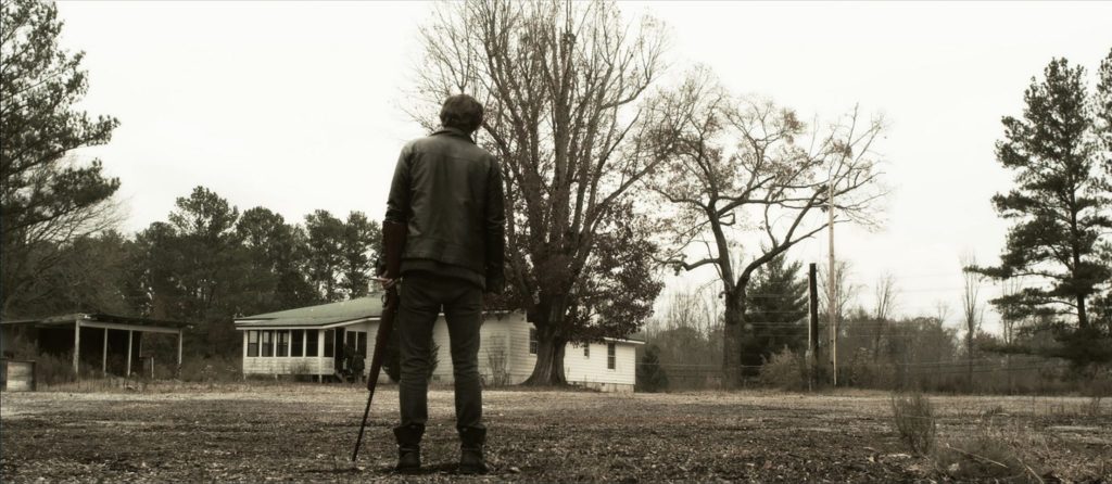 Ein bewaffneter Fremder steht vor einem einsamen Haus.