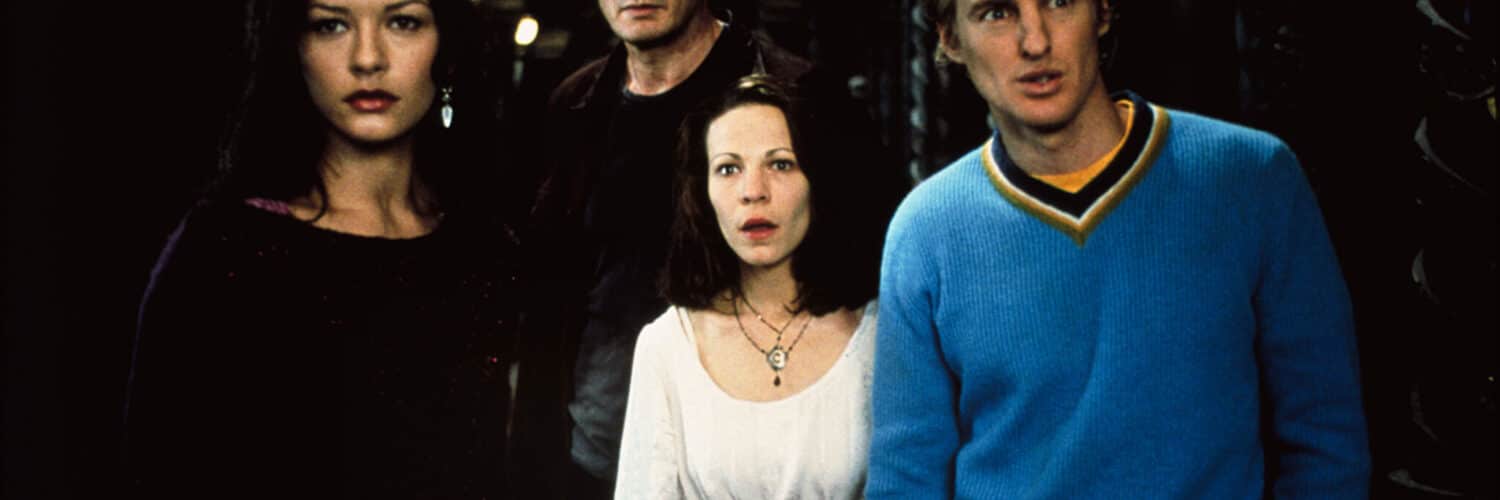 Catherine-Zeta Jones, Liam Neeson, Liliy Taylor und Owen Wilson aus Das Geisterschloss tragen Alltagskleidung und stehen in einem dunklen Flur mit flackerndem Kerzenlicht. Sie schauen entsetzt und überrascht, was um sie herum merkwürdiges passiert.