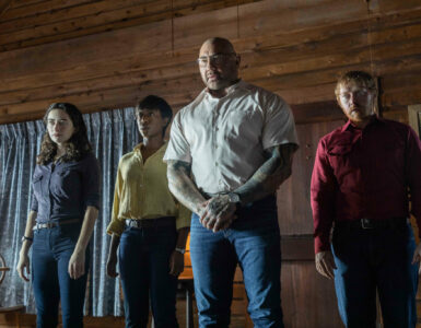 Die vier Invasoren stehen in der Hütte und schauen auf die Protagonisten, die sich hinter der Kamera befinden. In Knock at the Cabin.