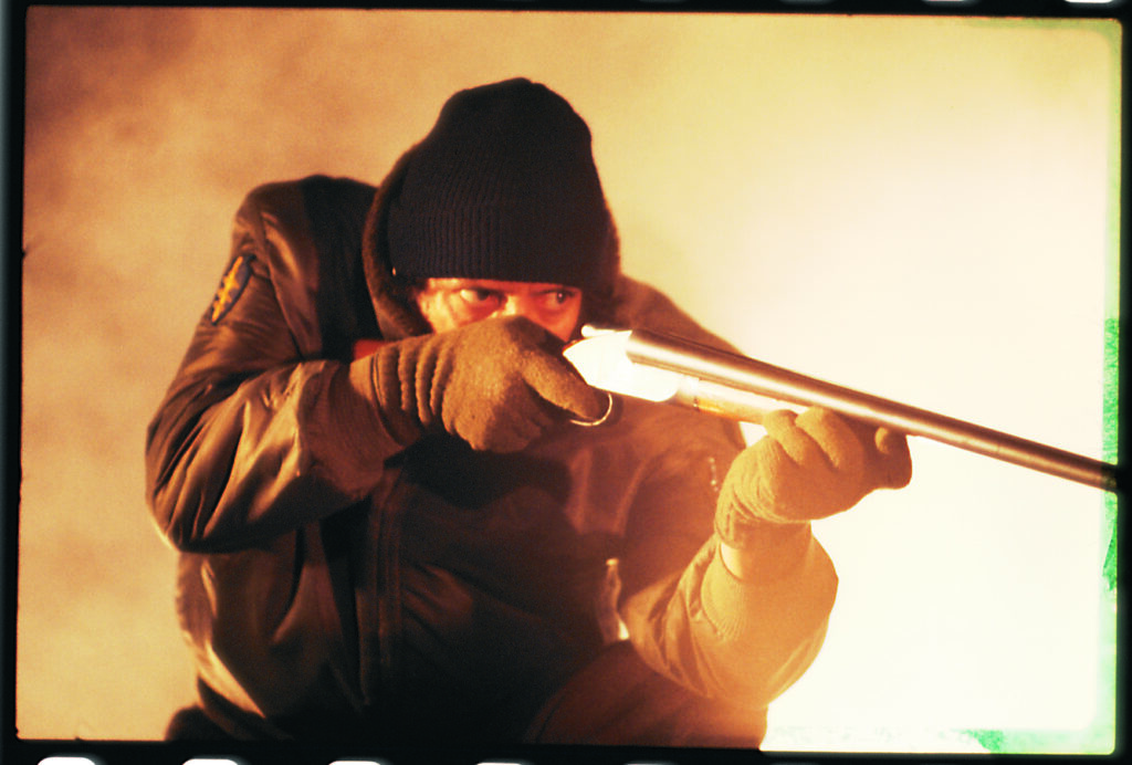 Joe Spinell als Frank Zito zielt hockend mit gezücktem Gewehr auf sein Opfer.
