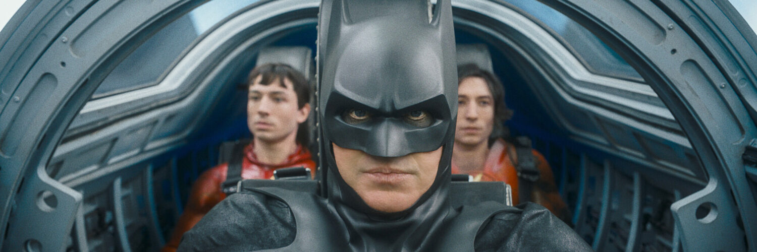In der Bildmitte im Vordergrund ist ein Mann in einem schwarzen Cape zu sehen. Er sitzt mit zwei gleichaussehenden Menschen in einem Fluggerät. Der Schauspieler Michael Keaton ist als Batman zu erkennen, die beiden Doppelgänger rechts und links neben im sind The Flash, der von Ezra Miller verkörpert wird.