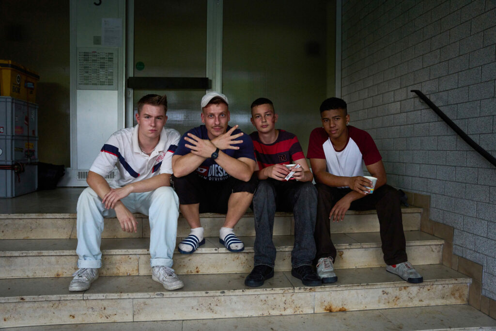 Die Darsteller von Lukas, Sanchez und Julius sitzen gemeinsam mit Felix Lobrecht auf einer Treppe, Lobrecht macht ein Handzeichen