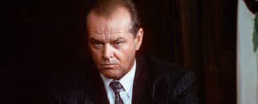 Gittes (Jack Nicholson) lunzt grimmig in Nahaufnahme und faltet seine Hände ineinander. Er trägt einen dunkelgrauen Anzug mit weißen Streifen, ein weißes Hemd und eine Krawatte.