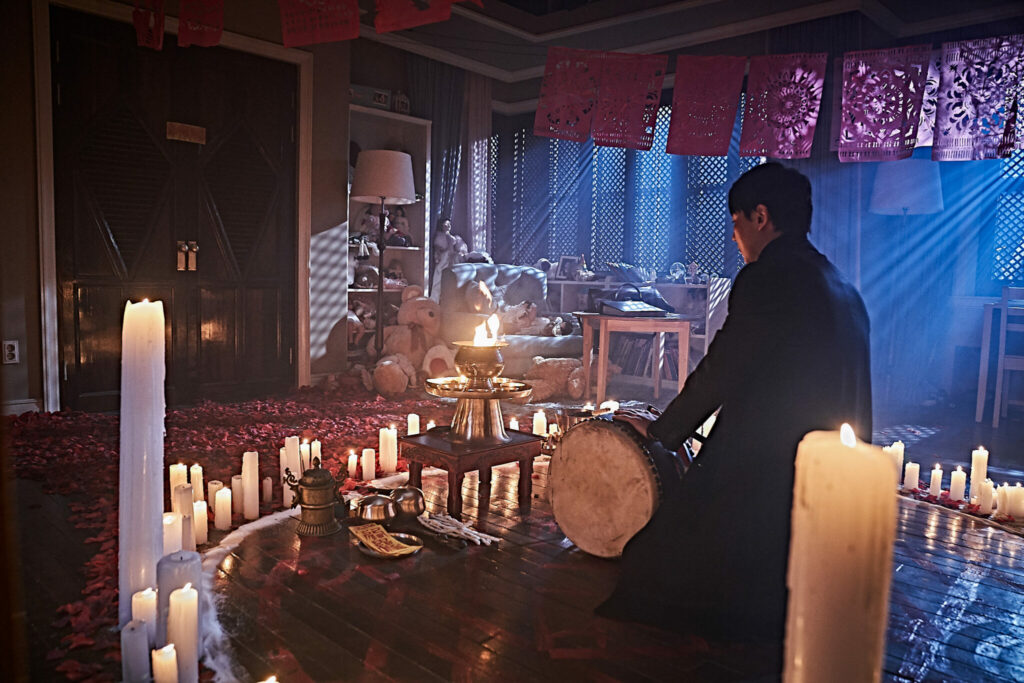 Kyung-hoon sitzt in einem Kreis von Kerzen mit einer Trommel in der Hand in The Closet