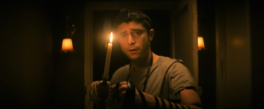 Yakov (Dave Davis) durchschreitet in THE VIGIL mit einer Kerze die Dunkelheit im mysteriösen Haus des Verstorbenen.