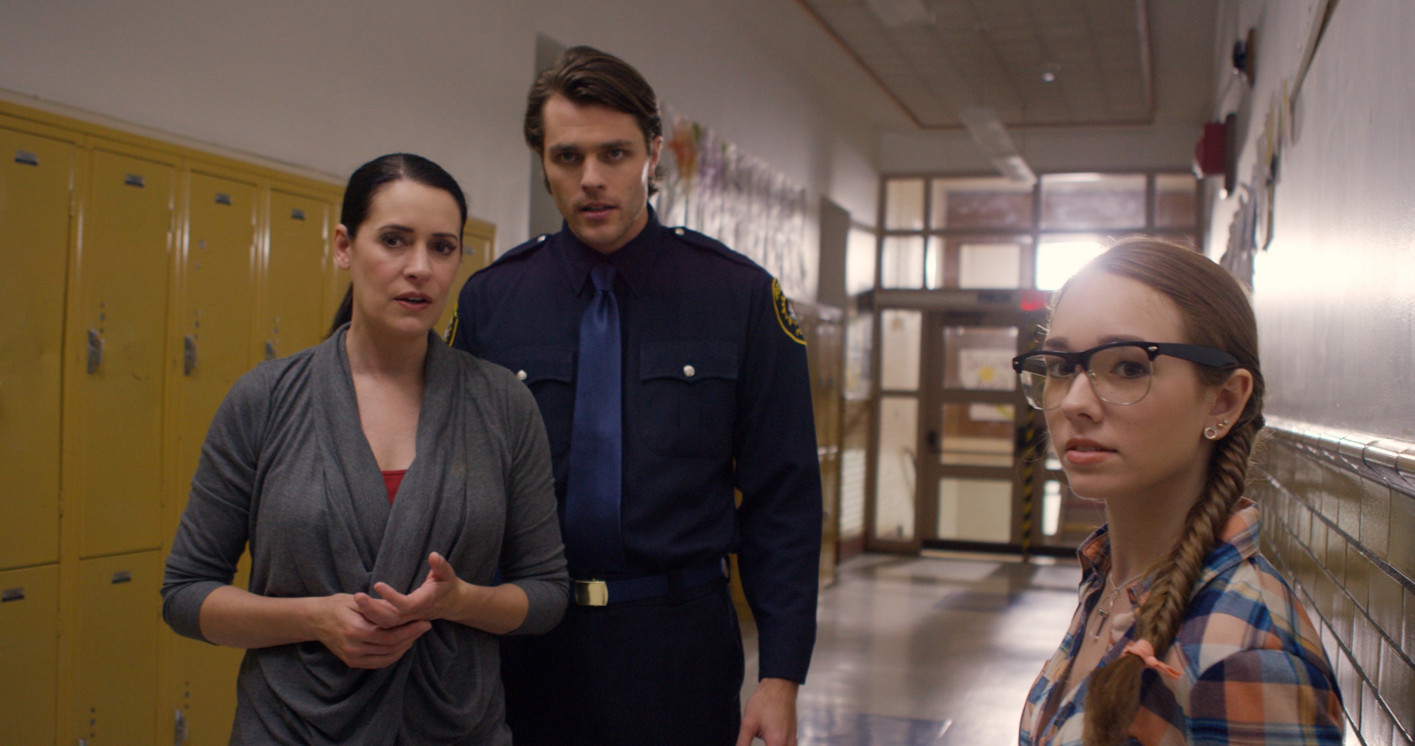Paget Brewster als Strauss und Holly Taylor als Claire stehen mit einem Polizisten im Gang einer Schule in The Witch Files.