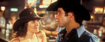 Debra Winger als Sissy blickt John Travolta als Bud Davis in "Urban Cowboy" leidenschaftlich an, während sich dieser an einem Bartresen mit ihr unterhält.