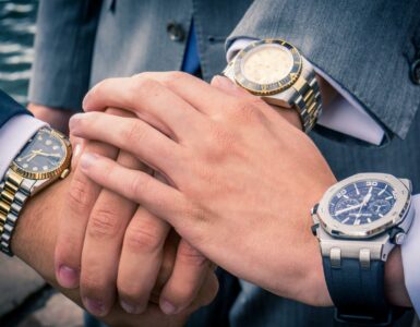 Drei Männer mit Armbanduhren, die die Hände übereinanderlegen