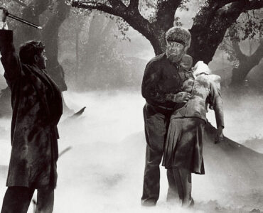 Der Wolfsmensch hält im nebligen, kargen Wald seine Geliebte Gwen, doch neben ihm erhebt sein Vater den Stock, um ihn zu töten - Universal Horror Filme