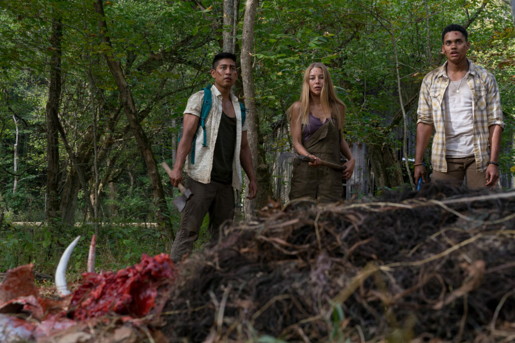 Jen, Darius und Luis stehen mit gezückten Waffen vor einer Leiche mit zerschmettertem Schädel