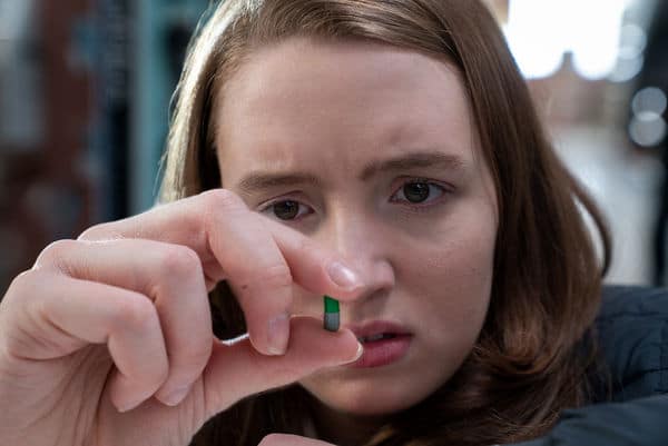 Chloe (Kiera Allen) schaut sich besorgt eine grüne Pille an, die sie zwischen den Fingern hält.