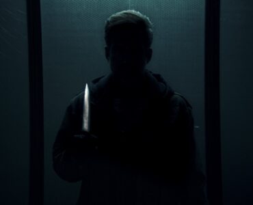 Auf dem Bild erkennt man eine Silhouette des Serienkiller "Der Cellist", wie er vor der Kamera mit einem Messer steht - Dark Glasses